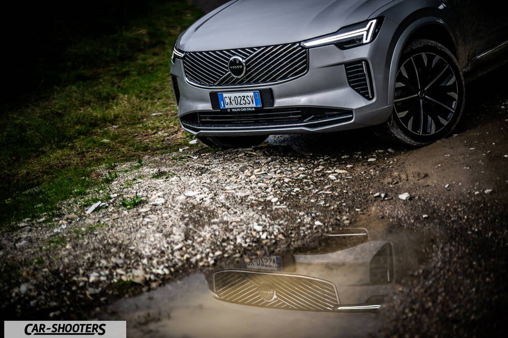 Volvo XC90 2025 – front three-quarter, silver on a gravel path with puddle reflection