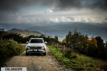 Volvo XC90 2025 – front three-quarter, silver on a dirt road against a mountain backdrop