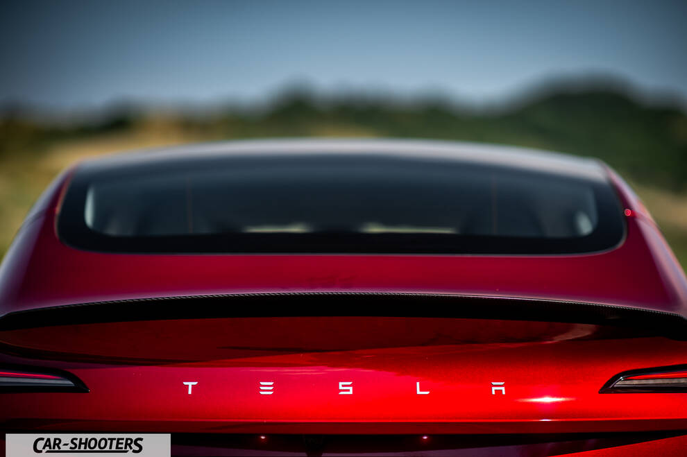 Tesla Model 3 Performance – rear view, red metallic against a blurred outdoor backdrop
