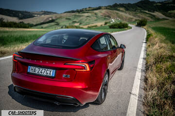 Tesla Model 3 Performance – rear three-quarter, red metallic on a winding country road